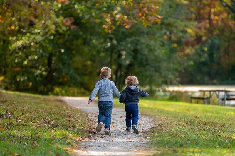 Dwoje dzieci idzie parkową alejką, widok od tyłu